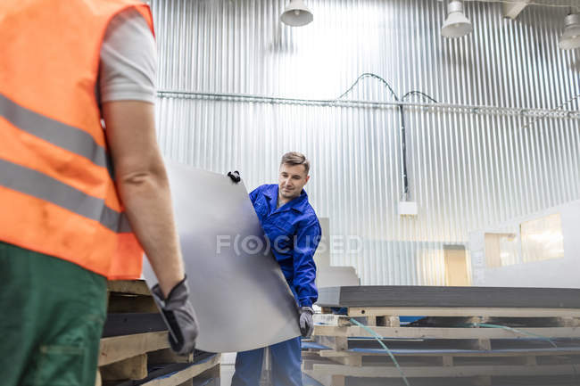 Trabajadores que llevan chapa metálica en fábrica - foto de stock