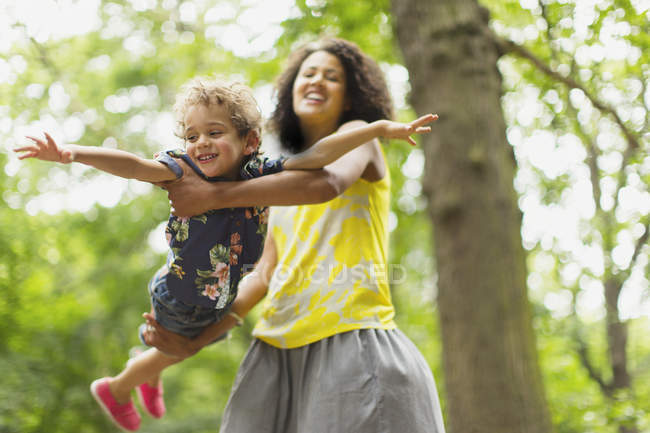 Playful mother flying son under tree — Stock Photo