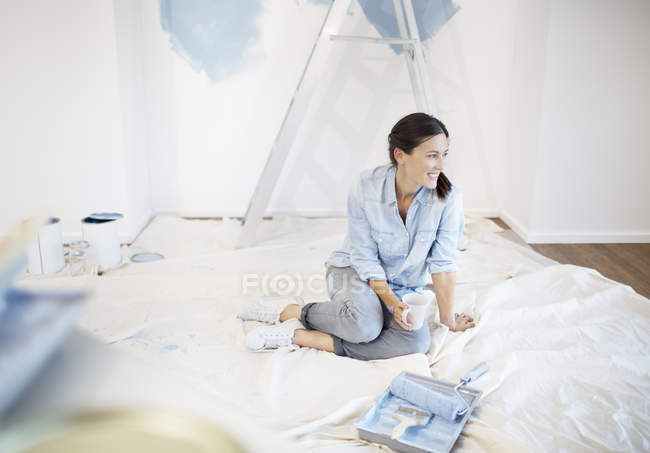 Woman drinking coffee surrounded by painting supplies — Stock Photo
