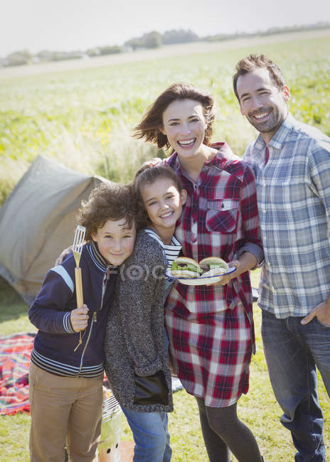Retrato família sorridente com hambúrgueres grelhados no acampamento ensolarado — Fotografia de Stock
