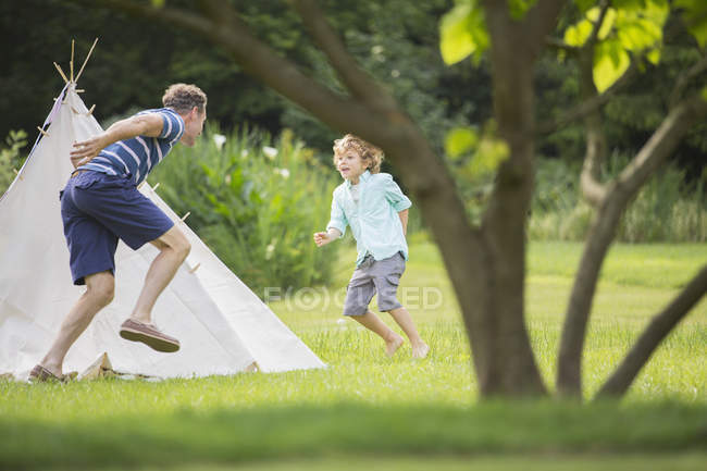 Father chasing son around teepee in backyard — Stock Photo
