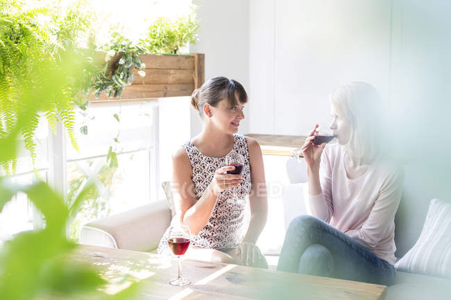 Women drinking wine and talking on cafe sofa — Stock Photo