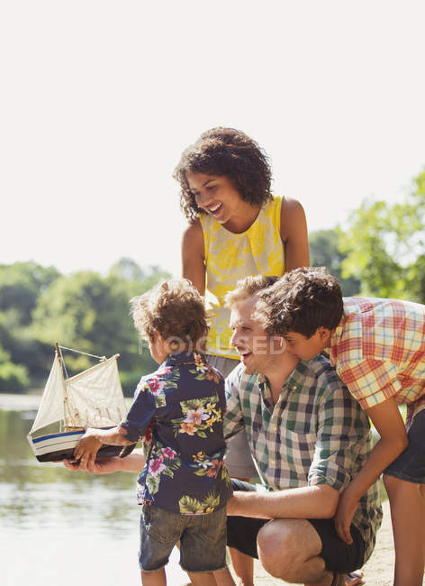 Famiglia con barca a vela giocattolo sul lungolago soleggiato — Foto stock
