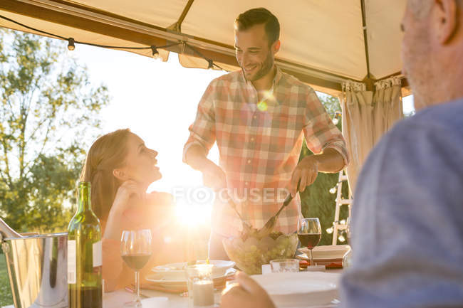 Young man serving salad to wife at sunny patio table — Stock Photo