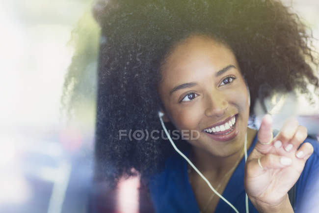 Mujer sonriente con afro y auriculares dibujando en forma de corazón en la ventana del autobús - foto de stock