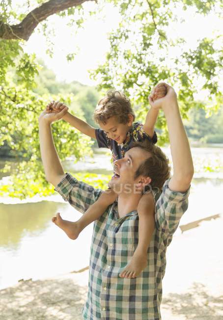 Pai brincalhão carregando o filho em ombros no lago — Fotografia de Stock