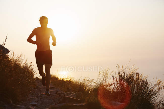 Silhouette de l'homme courant sur le sentier avec coucher de soleil océan en arrière-plan — Photo de stock