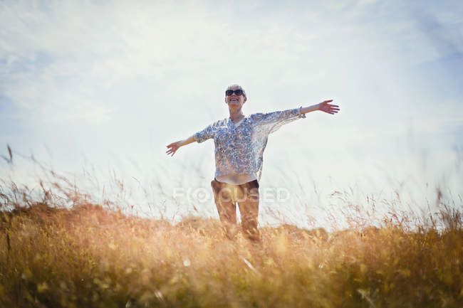 Mujer mayor despreocupada corriendo con los brazos extendidos en el campo soleado - foto de stock