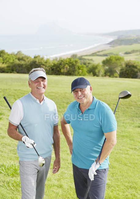 Hommes âgés souriant sur le terrain de golf surplombant l'océan — Photo de stock