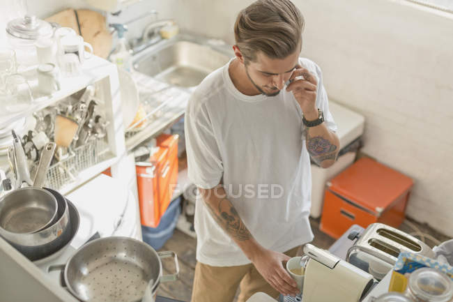 Homem usando máquina de café expresso e falando no telefone celular na cozinha do apartamento — Fotografia de Stock