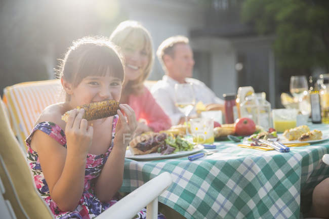 Девушка ест кукурузный початок за столом во дворе — стоковое фото