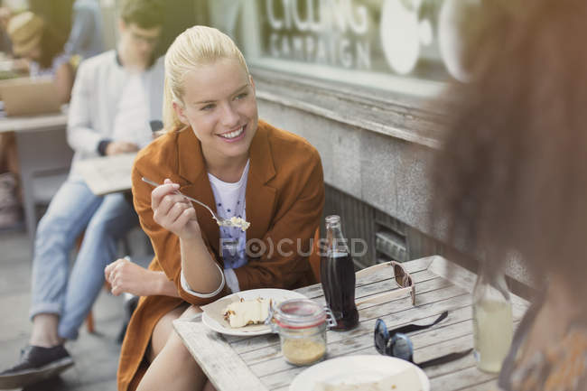 Mujer rubia sonriente comiendo postre en el café de la acera - foto de stock
