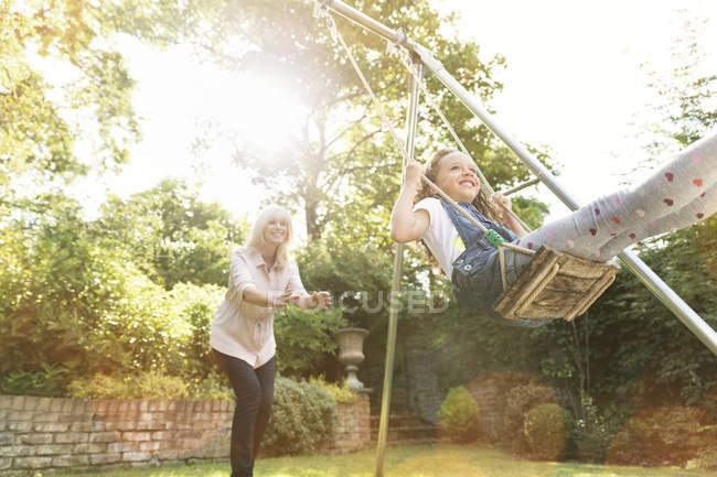 Grandmother pushing granddaughter on swing in backyard — Stock Photo