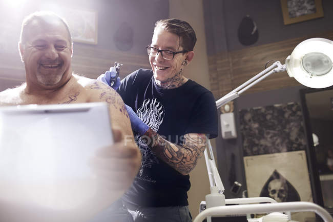 Lächelnder Mann mit digitalem Tablet bekommt Schultertätowierung im Studio — Stockfoto