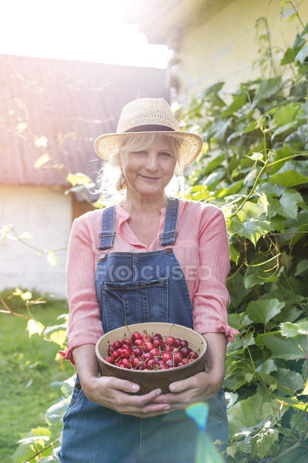 Retrato mujer sonriente en overoles sosteniendo cerezas cosechadas - foto de stock
