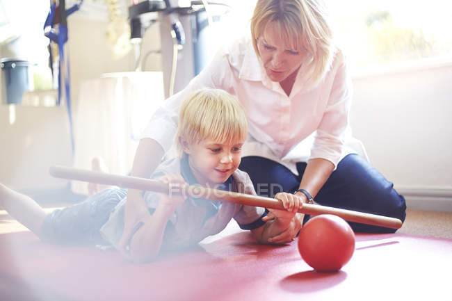 Физиотерапевт направляет мальчика катать мяч с палкой — стоковое фото