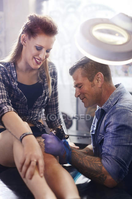 Tatuaje artista tatuar mujer muslo en estudio - foto de stock