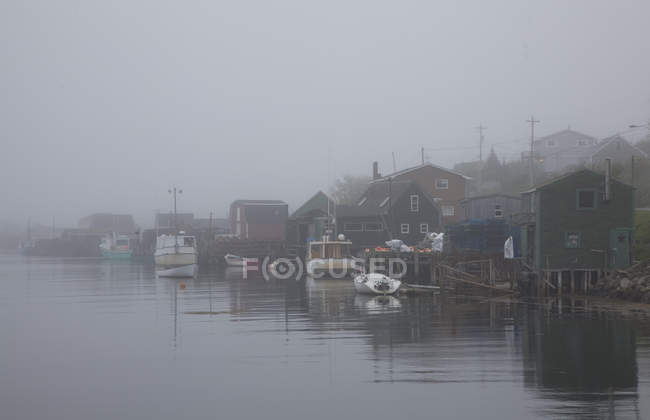 Fog surrounding houses and boats on river — Stock Photo