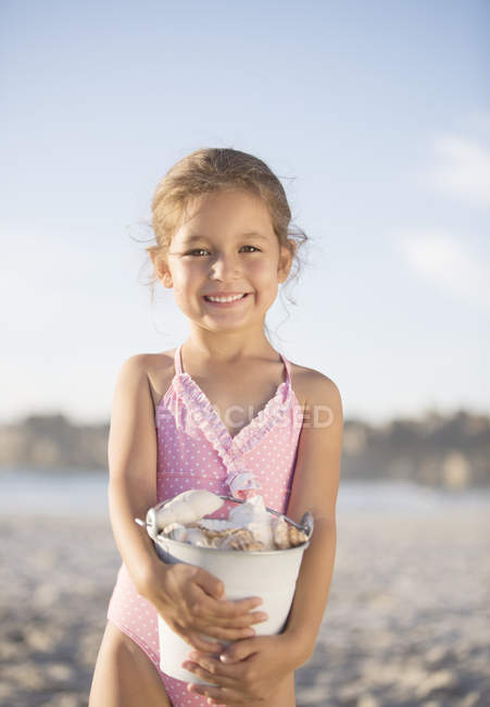 Menina segurando balde de conchas na praia — Fotografia de Stock