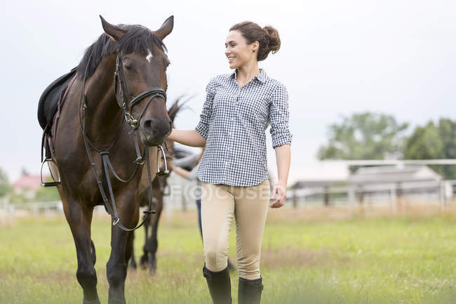 Улыбающаяся женщина, ходящая лошадь на сельском пастбище — стоковое фото