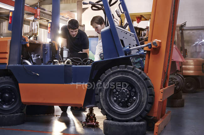 Mecânica examinando empilhadeira na oficina de reparação de automóveis — Fotografia de Stock