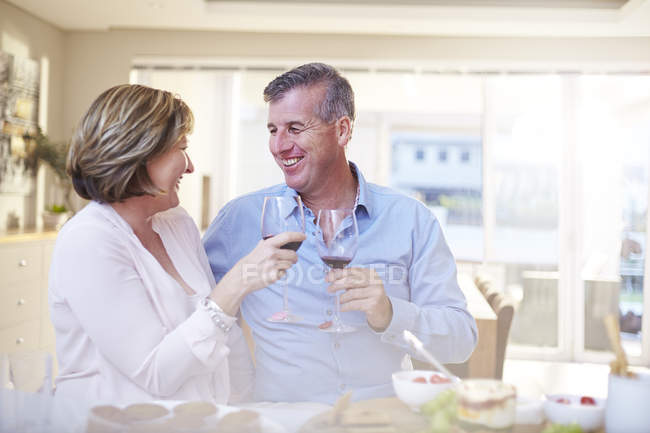 Sonriente pareja tostando copas de vino tinto en la cocina - foto de stock