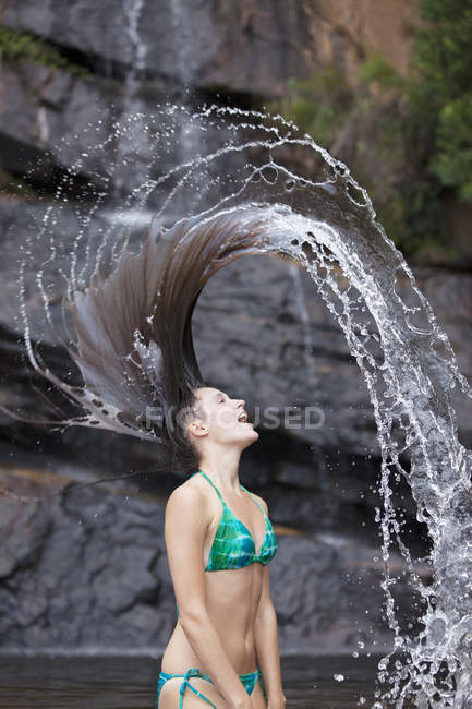 Mujer volteando el pelo en agua contra roca - foto de stock