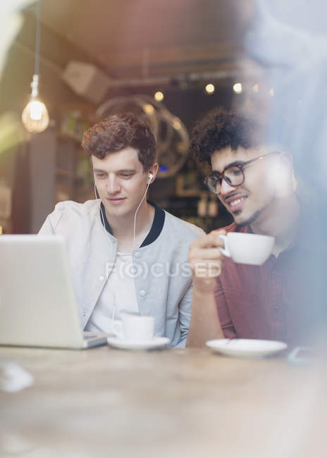 Друзі п'ють каву і використовують ноутбук у кафе — стокове фото