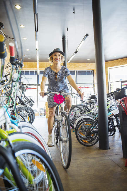 Mulher sorridente andando de bicicleta na loja de bicicletas — Fotografia de Stock