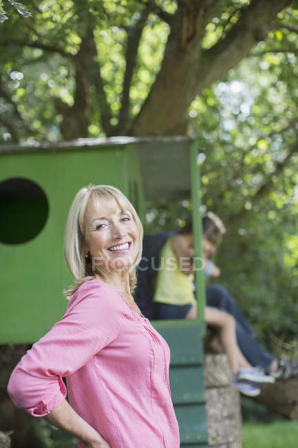 Mulher feliz sorrindo com árvore casa no fundo — Fotografia de Stock