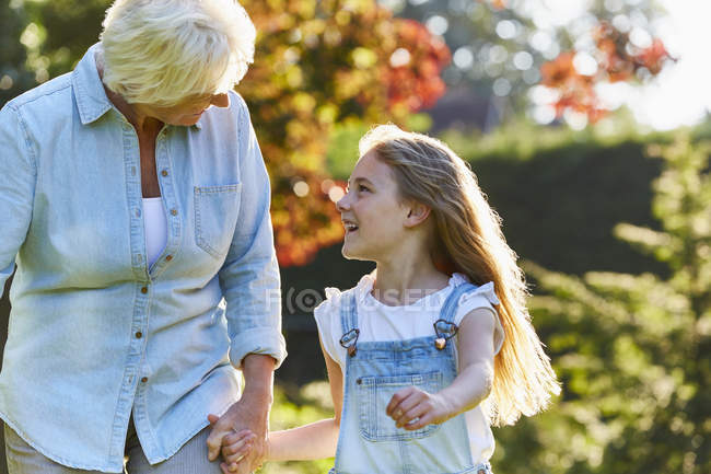 Grandmother and granddaughter holding hands and walking in sunny garden — Stock Photo