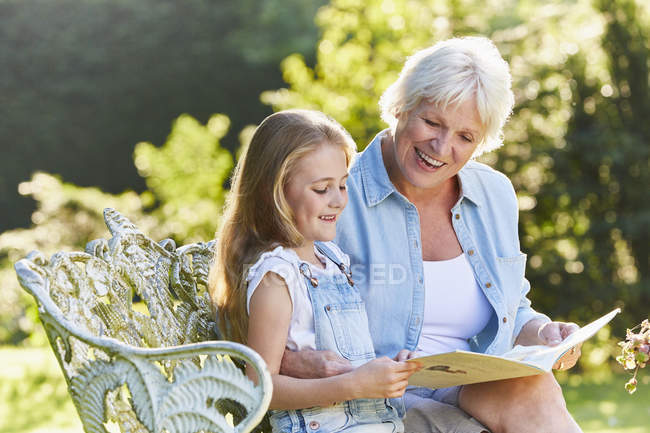 Бабуся читає з онукою на садовій лавці — стокове фото