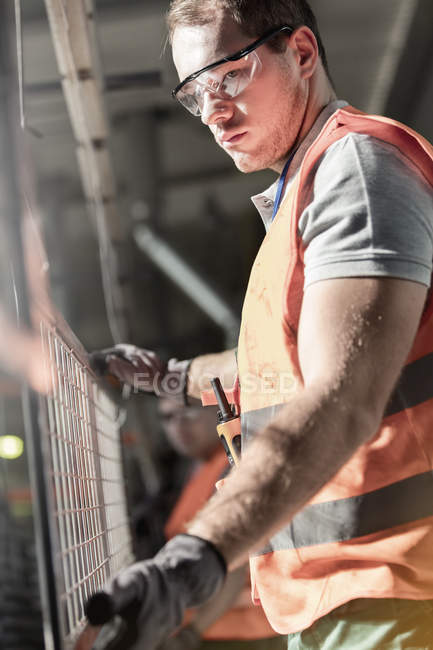 Trabalhador focalizado segurando parte de aço na fábrica — Fotografia de Stock