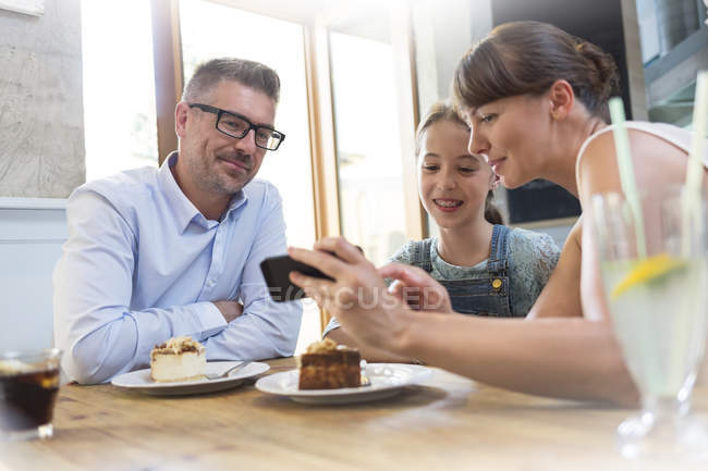 Family with cell phone eating dessert at cafe table — Stock Photo