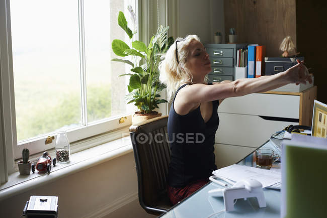 Молода жінка розтягує руки за столом в домашньому офісі — стокове фото