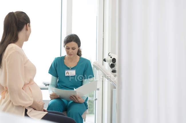 Медсестра і вагітна пацієнтка розглядають медичну карту в кабінеті огляду — стокове фото