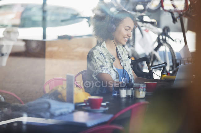 Усміхається жінка з навушниками в ноутбук в кафе — стокове фото