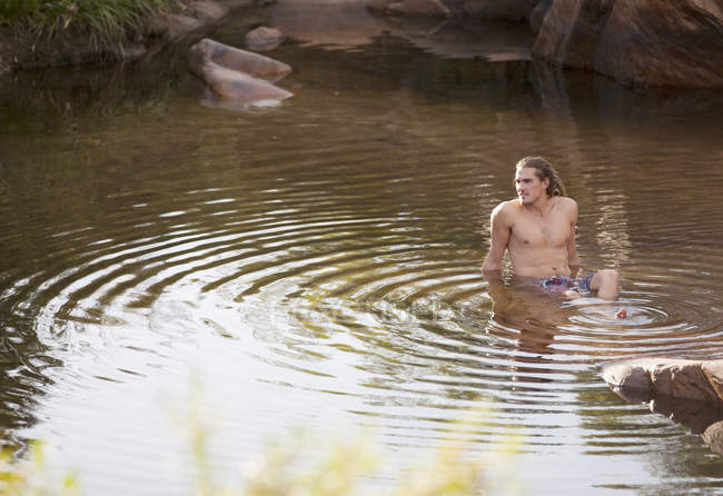 Hombre sentado en el agua del río durante el día - foto de stock