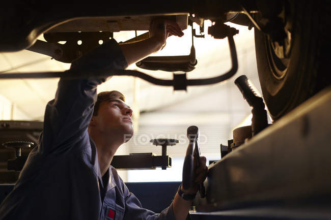 Mecánico trabajando bajo el coche en taller de reparación de automóviles - foto de stock