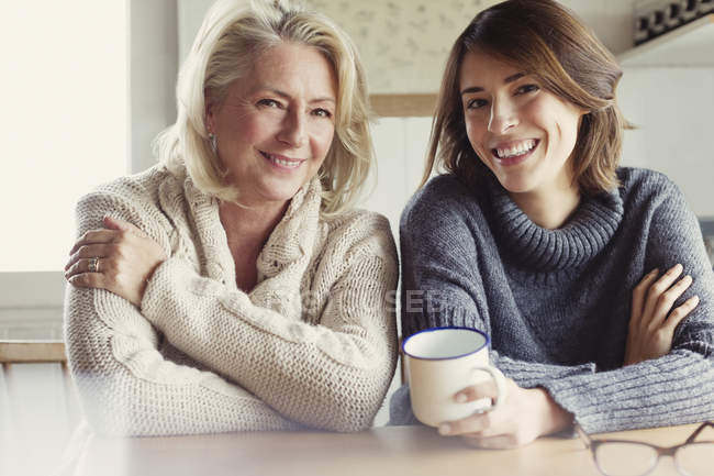 Портрет усміхненої матері і дочки в светрах, що п'ють каву на кухні — стокове фото