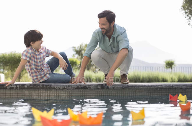 Father and son watching origami boats in swimming pool — Stock Photo