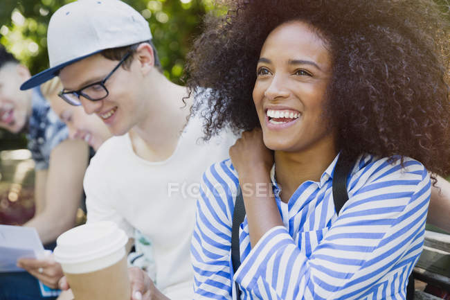 Mujer sonriente con afro bebiendo café con amigos al aire libre - foto de stock