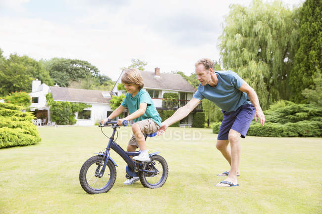 Father pushing son on bicycle in backyard — Stock Photo