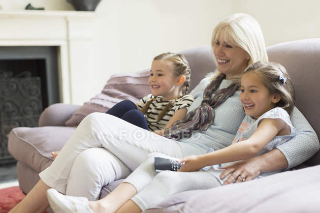 Grandmother and granddaughters watching TV on living room sofa — Stock Photo