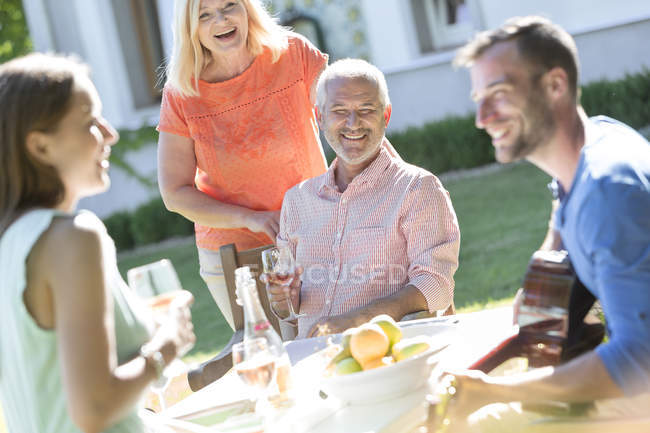 Familia bebiendo vino y tocando la guitarra en la soleada mesa del patio - foto de stock
