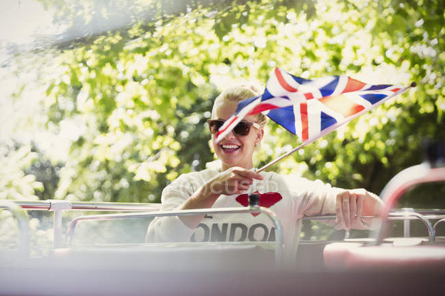 Mulher sorridente acenando bandeira britânica em ônibus de dois andares — Fotografia de Stock