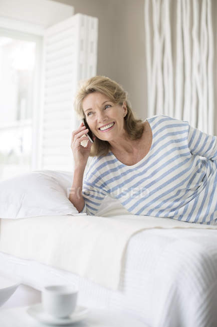 Older woman talking on cell phone on bed — Stock Photo