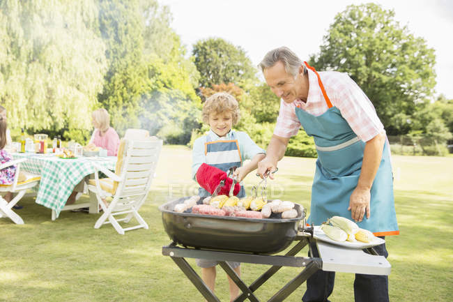 Grandfather and grandson grilling meat and corn on barbecue — Stock Photo