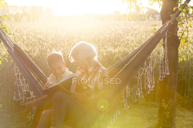 Grandmother and grandson reading book in sunny rural hammock — Stock Photo