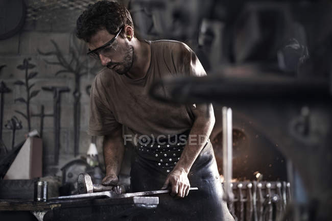 Blacksmith hammering iron at anvil in forge — Stock Photo